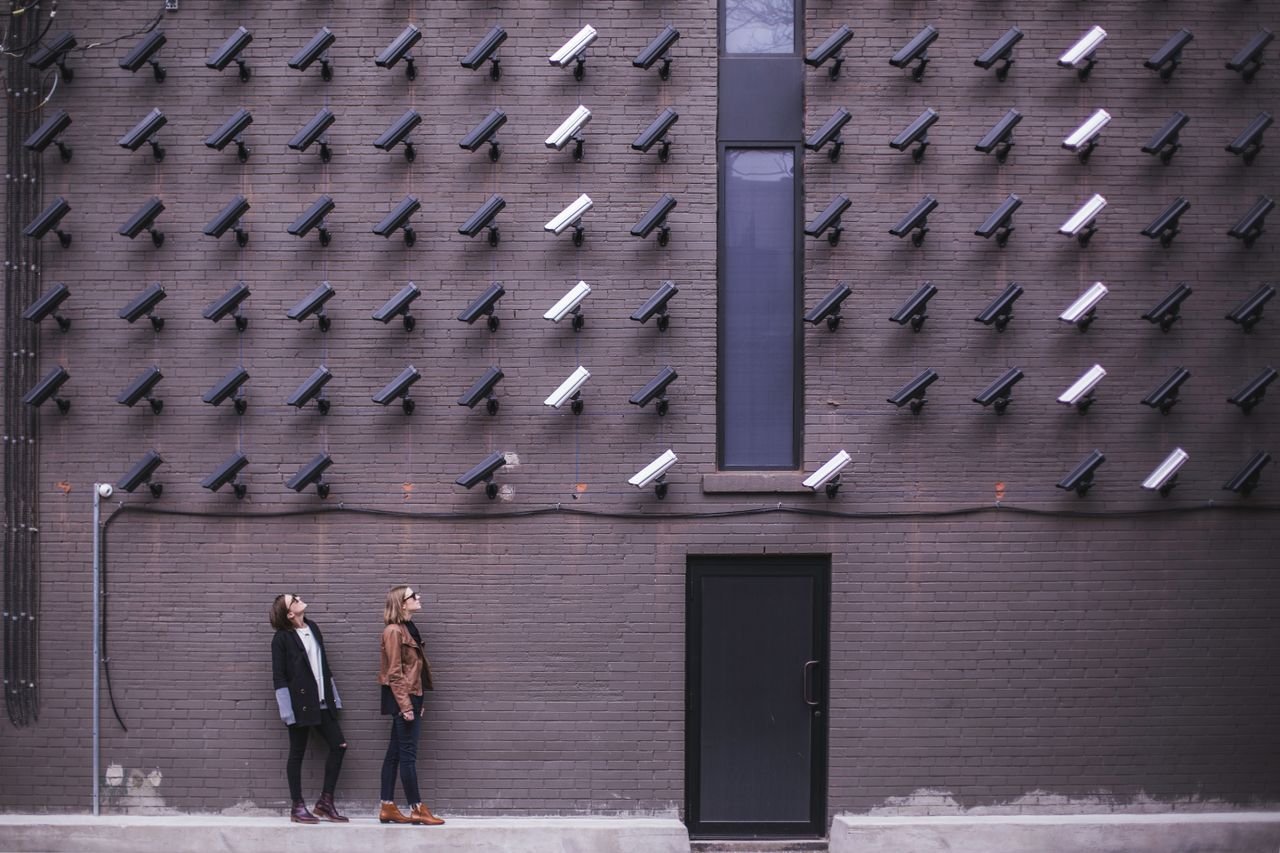 Mastering the First Impression: Your intriguing post title goes here Women observing a wall covered with numerous security cameras in an urban setting, showcasing modern surveillance.